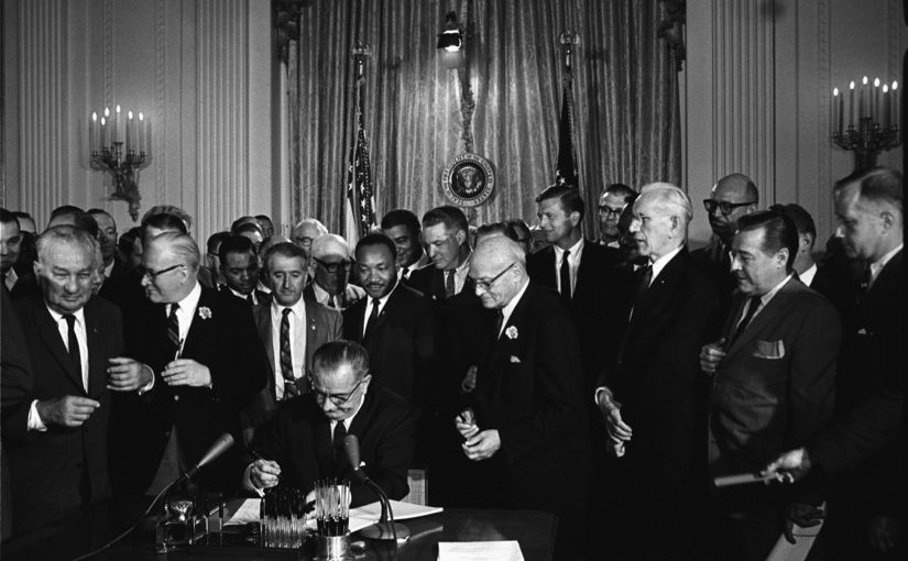 President Lyndon B. Johnson signs the 1964 Civil Rights Act as Martin Luther King, Jr., and others, look on. (Public Domain)
