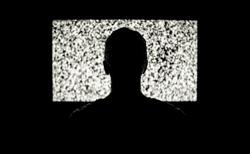 Silhouette of the back of someone's head in front of a television.
