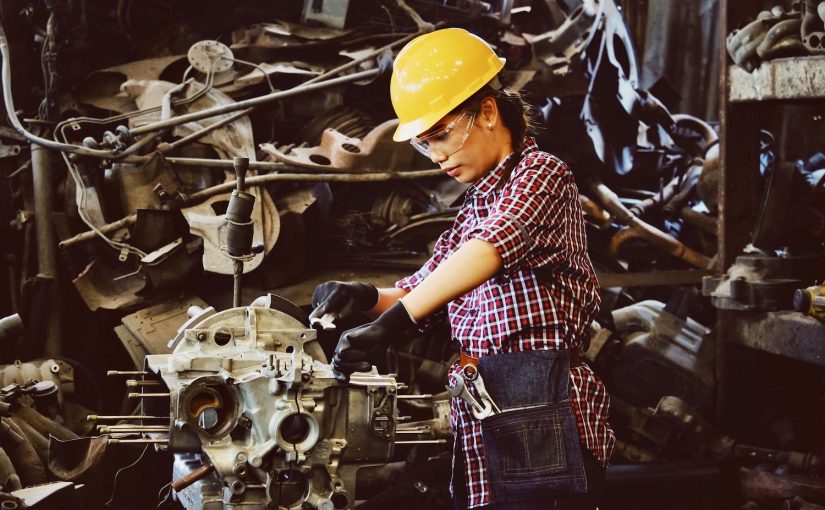 A picture of a woman reflectively and skillfully repairing an engine.